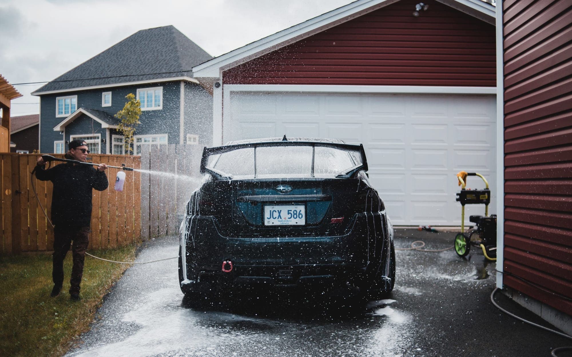Detailer pressure-washing an SUV on a residential driveway